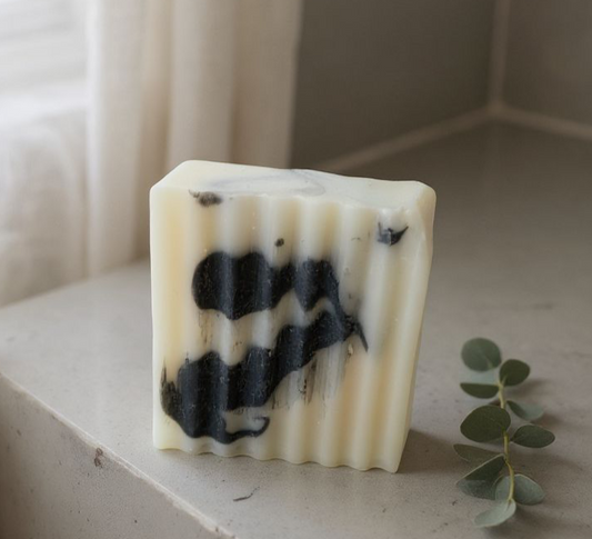 Bar of soap with charcoal specks on a light surface with a leaf